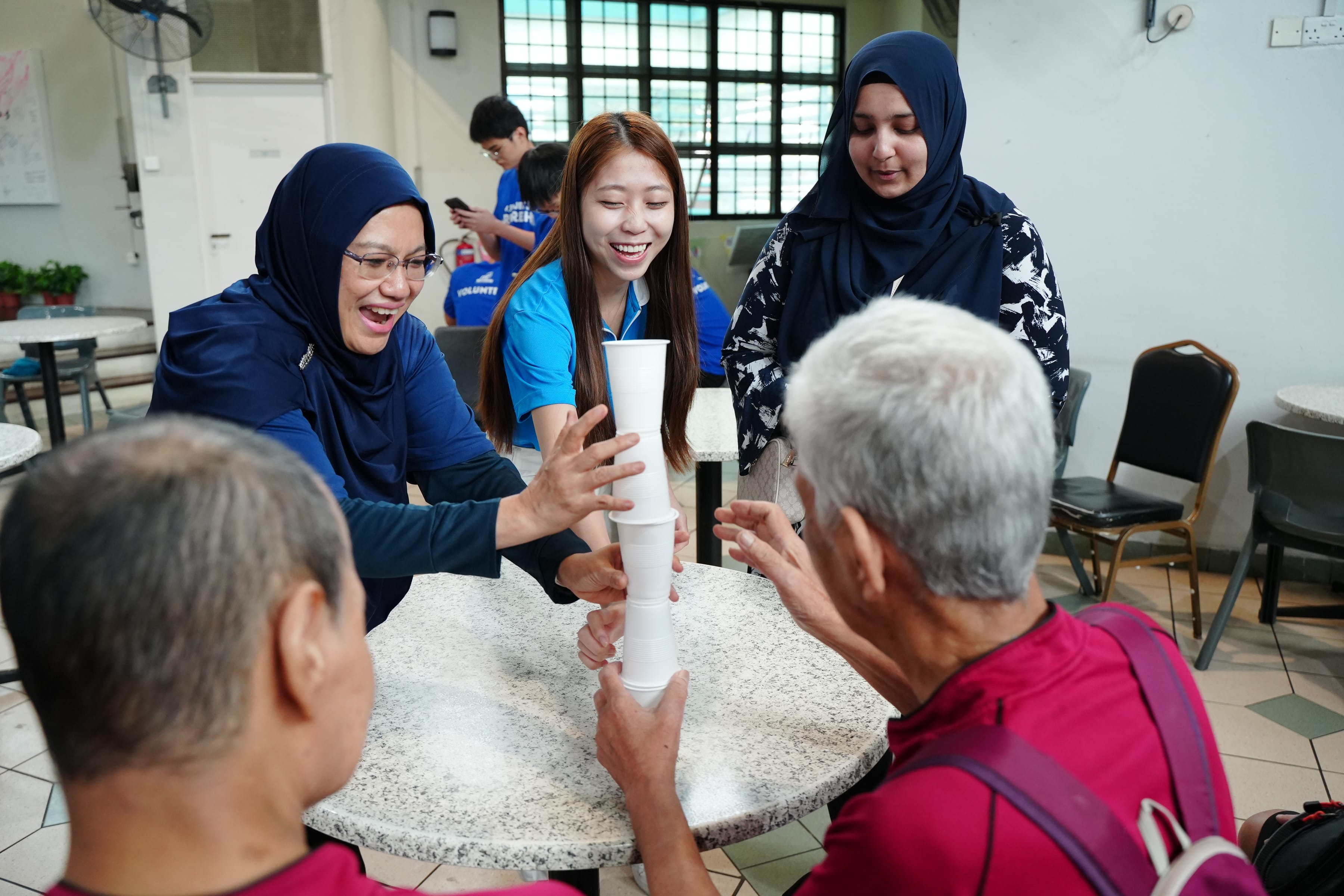 Three volunteers engaging two elderly individuals in a cup-stacking game.